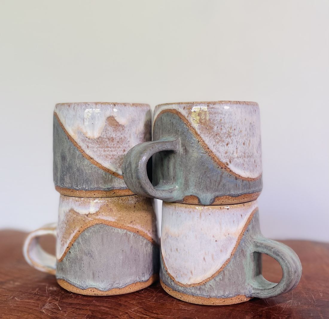 Four stacked mugs in grey-blue glaze over raw clay