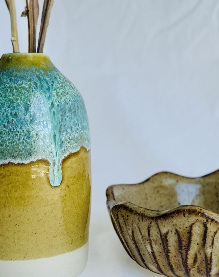 Vase with seafoam glaze dripping over gold, beside a carved scalloped bowl