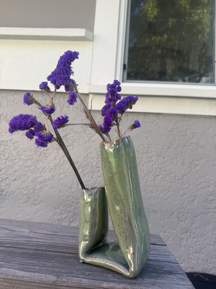 Sculpted two-chamber bud vase in glossy green holding purple statice