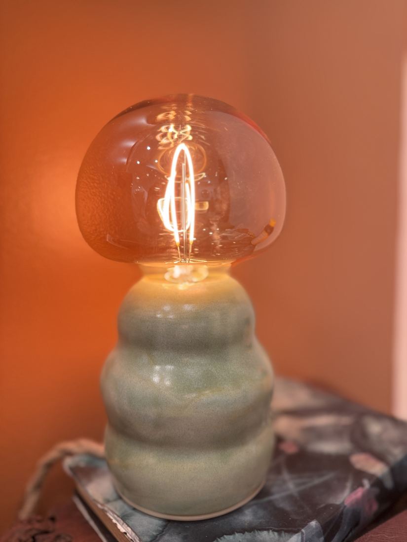 Lamp with a stacked sage-green ceramic base and a globe bulb, lit