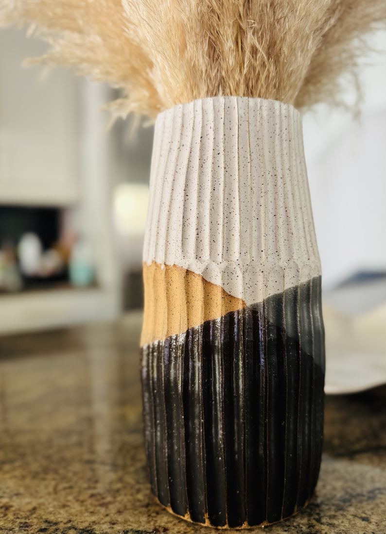 Tall ribbed vase in black, gold and speckled white holding pampas grass